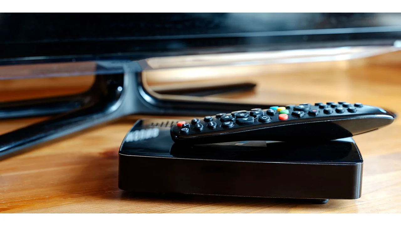 IPTV via AliExpress: de gevaren van goedkope boxen en abonnementen 1 Zwarte mediaspeler met afstandsbediening voor een televisie op een houten meubel.